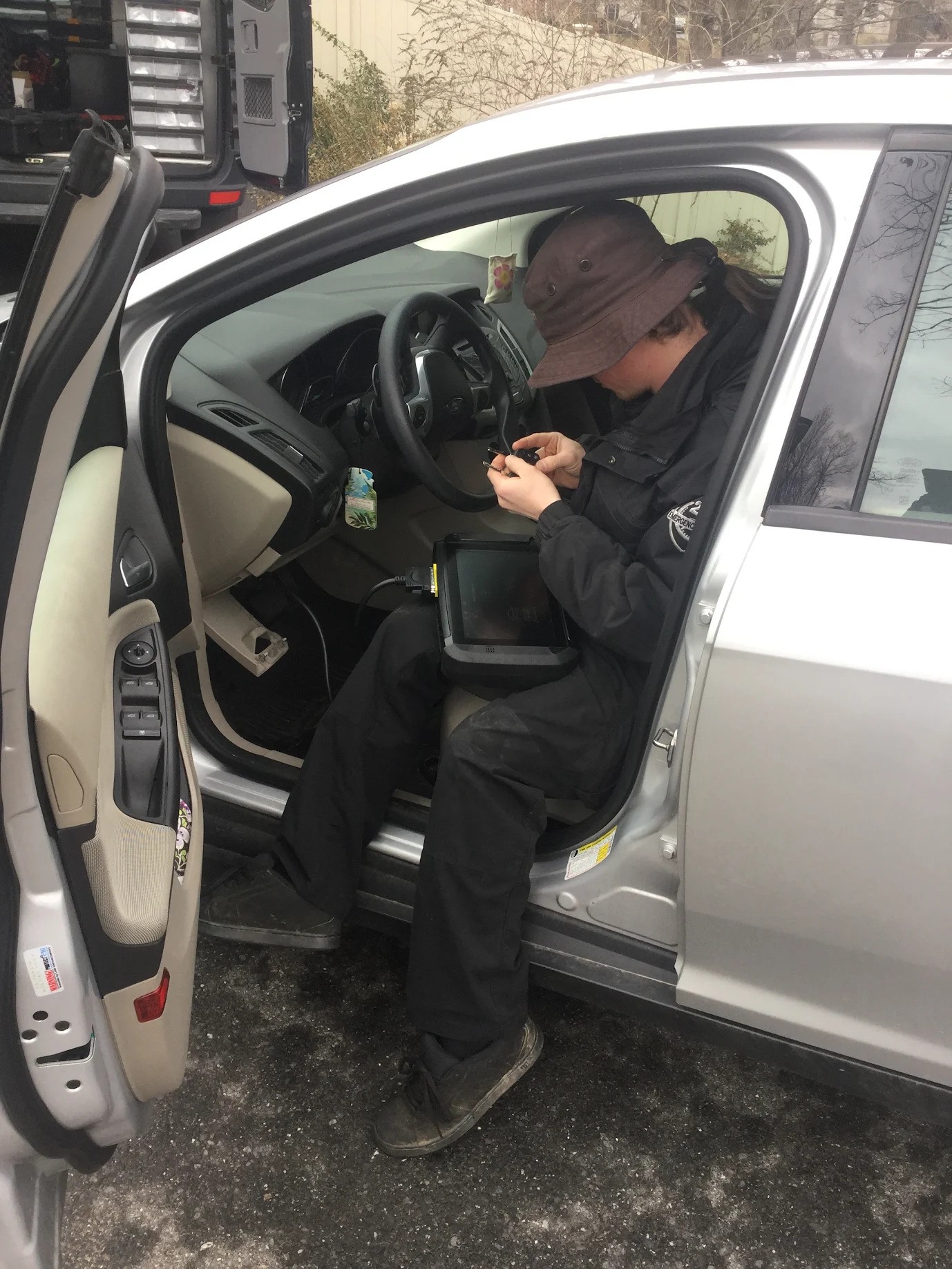 A locksmith fixing a car ignition with a car computer interface