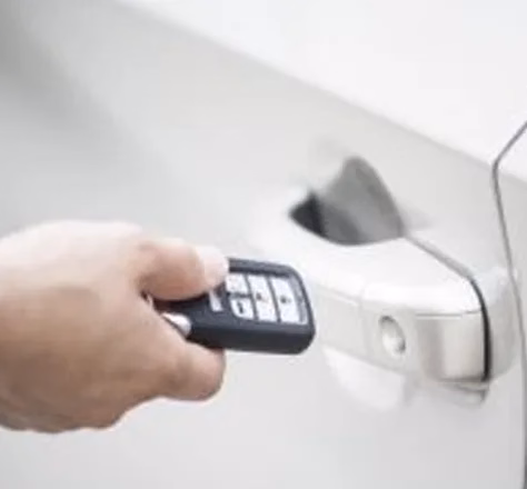 a hand holding a car door remote up to a car door handle